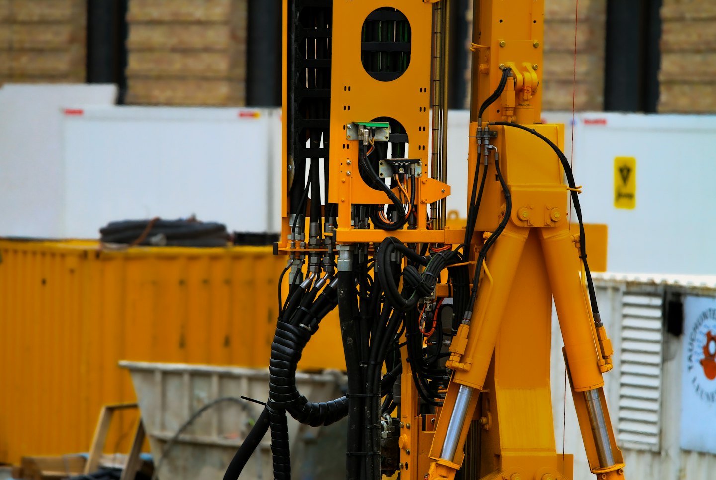 Gelbe Baumaschine aus Metall mit schwarzen Hydraulikschläuchen und Verkabelung.